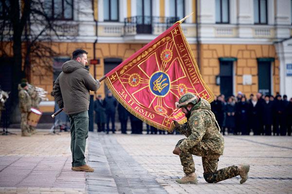  러시아의 우크라이나 침공 1년을 맞은 지난 24일, 우크라이나 수도 키이우에서 한 장교가 볼로디미르 젤렌스키(왼쪽) 대통령이 들고 있는 군부대 깃발에 입 맞추고 있다. [로이터]