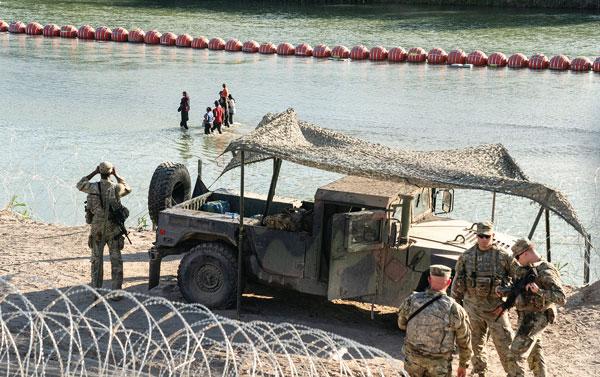  미국서 난민 신청을 희망하는 중남미 이민자들이 텍사스주 방위군이 감시하는 가운데 수중장벽이 설치된 리오그란데 강을 가로지르고 있다. [로이터]