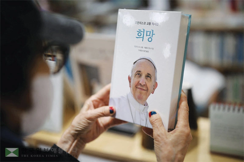 한인 천주교 신자가 21일 한국 명동 성당에서 프란치스코 교황의 자서전 ‘희망’(Hope)의 표지를 바라보며 교황의 선종을 애도하고 있다. [로이터]