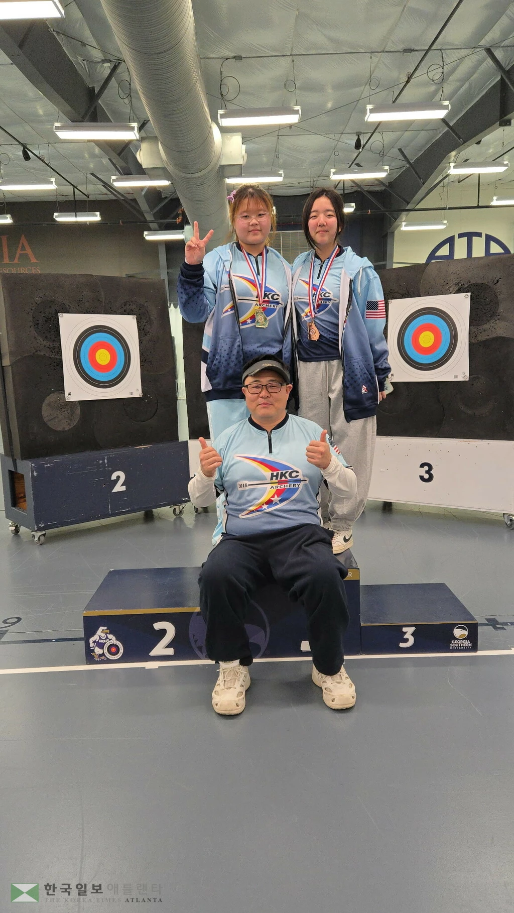 조지아주 양궁대회에서 메달에 입상한 이레 리, 하윤 최 학생이 HKC-양궁 감독과 함께 포즈를 취했다.