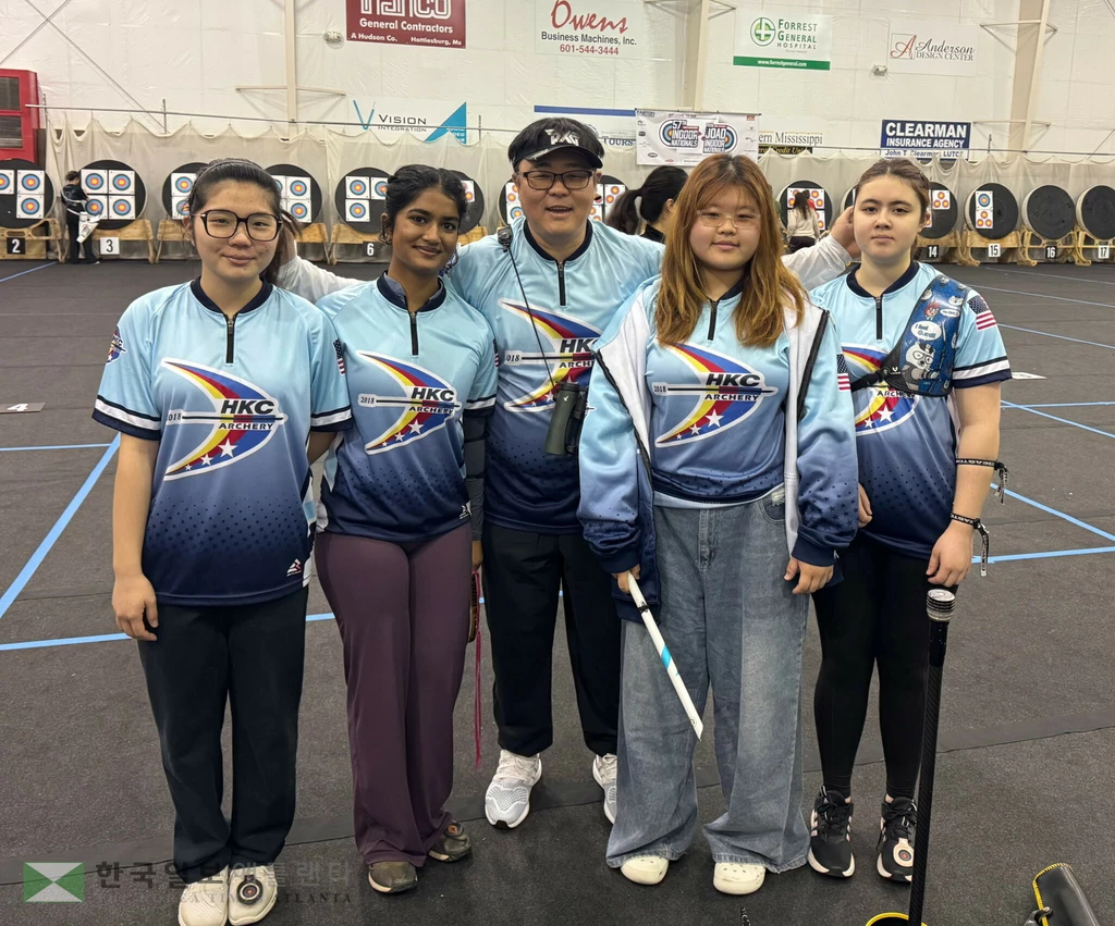 제57회 미국 실내양궁 내셔널 챔피언십에서 출전 선수 전원 상위권 진입의 쾌거를 이룬 HKC_ARCHERY 선수단과 지도자가 대회장 조준선 뒤에서 기념 촬영을 하고 있다.