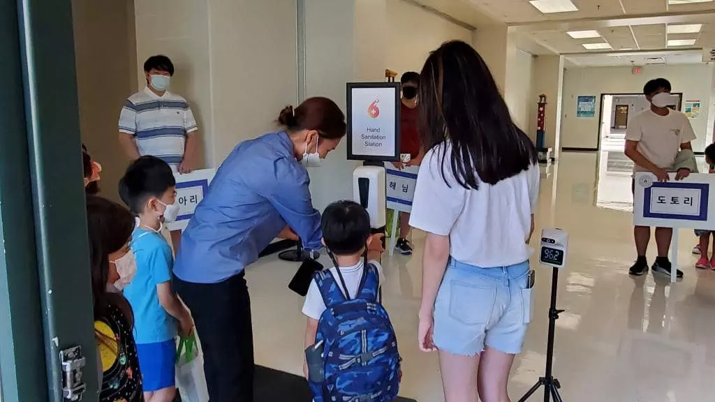 교사가 어린 학생의 발열체크와 손소독을 지도하고 있는 모습