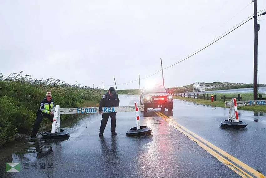 허리케인 헨리로 롱아일랜드 사우샘프턴의 한 도로가 침수되면서 지역 경찰관들이 차량진입 금지 표지판을 설치하고 있다.                                                                 <로이터>
