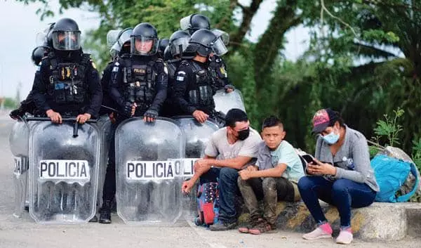 온두라스 이민자들이 16일 과테말라 경찰의 저지를 받고 길가에 앉아 있다. [로이터]