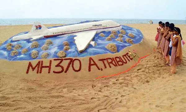  2014년 3월 25일 인도 동부 오디샤주의 한 해변에 설치된 말레이시아 여객기(MH370)와 탑승객들의 무사 귀환을 염원하는 모래 작품 근처에서 학생들이 간절한 기도를 올리고 있다. [로이터]
