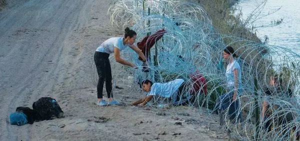  텍사스주 이글패스 지역에서 한 이민자 가족이 불법 입국을 막기 위해 텍사스주 방위군이 쳐놓은 철조망 사이를 위험을 무릅쓰고 통과하고 있다. [로이터]